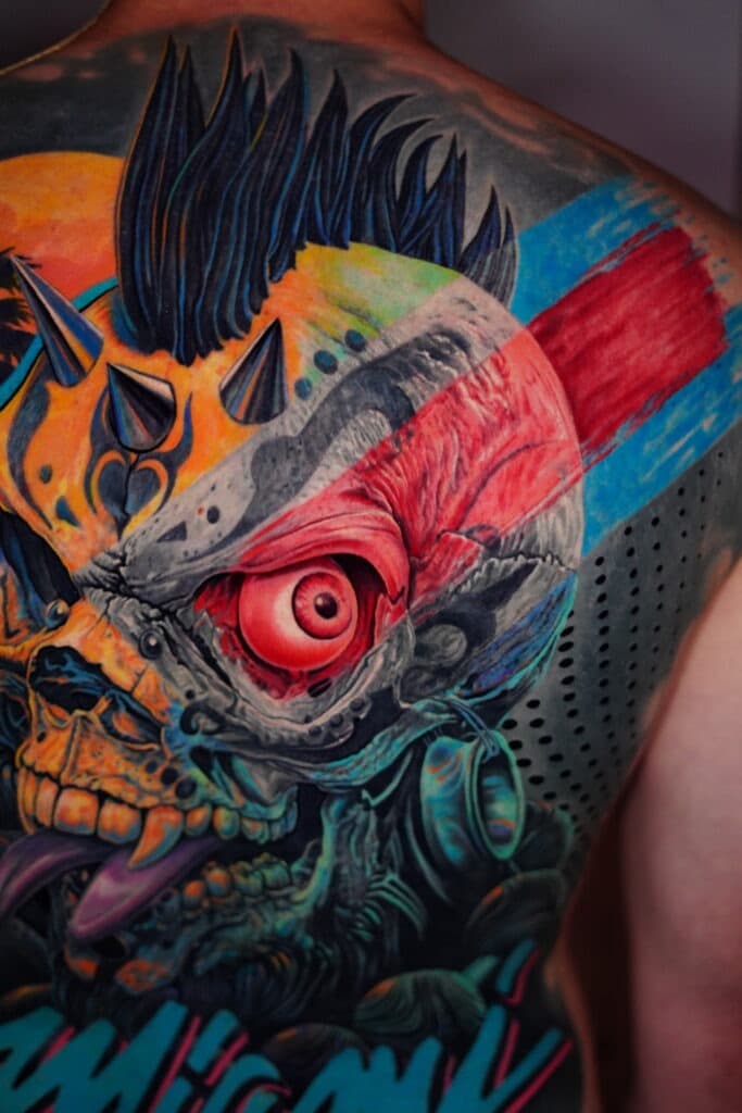 Colorful tattoo of a skull with a large red eye, black mohawk, and blue and orange details