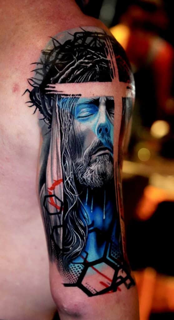 Upper-arm tattoo of Jesus with a crown of thorns, blue shading, and geometric black and red accents