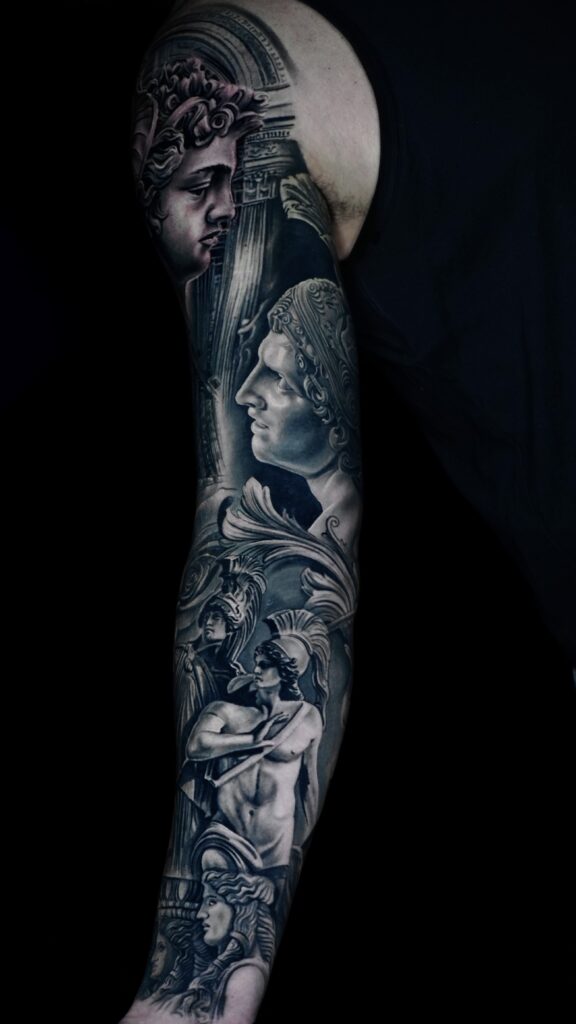 Black-and-gray sleeve tattoo with classical Greek statues, columns, and helmeted figures on an arm
