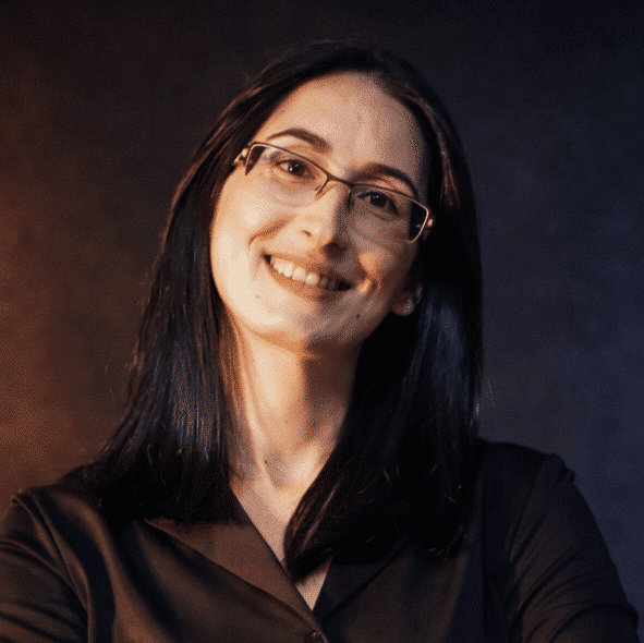 Smiling woman with glasses in a dark blouse against a studio background