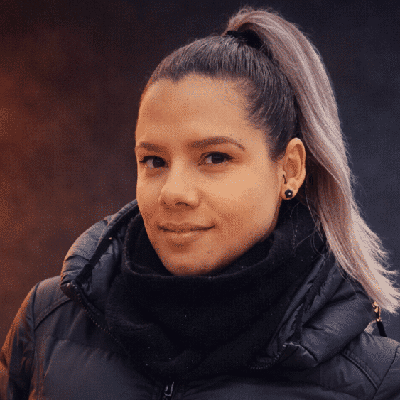 Woman with a high ponytail wearing a black puffer jacket and scarf, looking at the camera