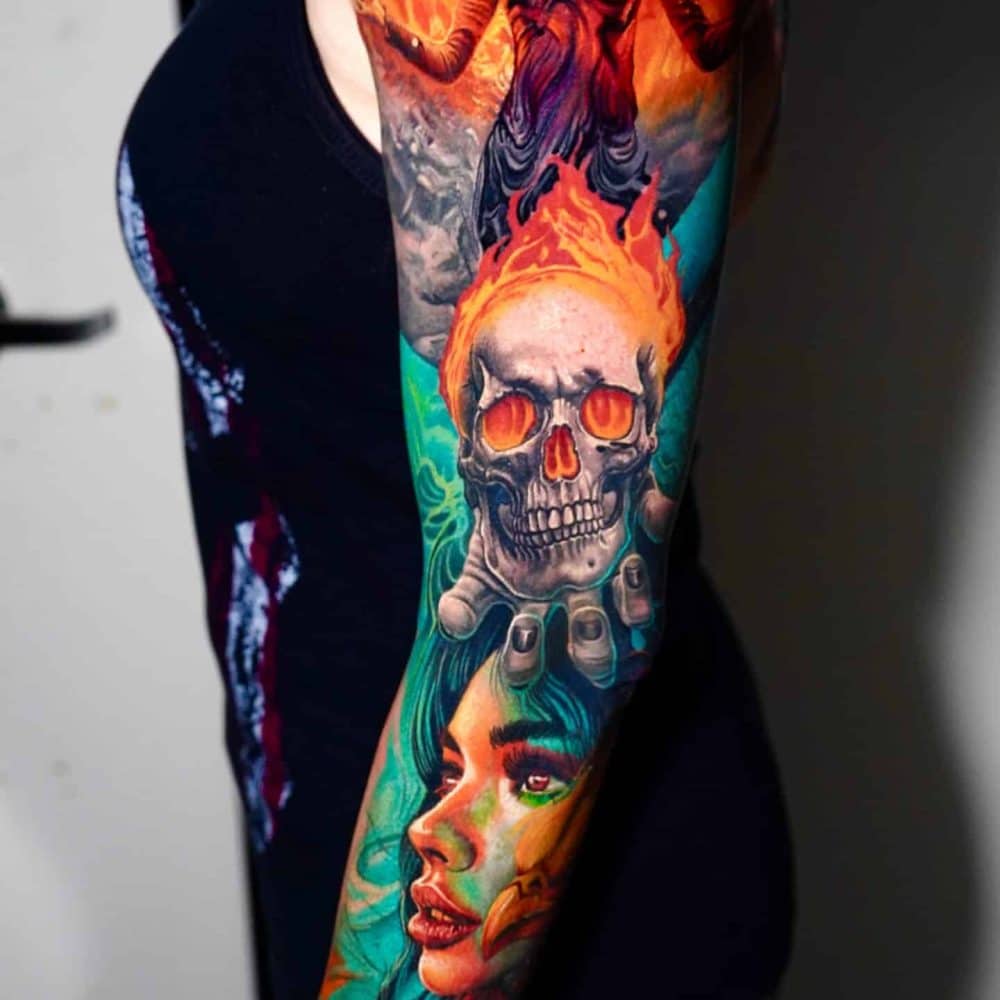 Colorful full-sleeve tattoo featuring a fiery woman, flaming skull, and a woman's face on the forearm