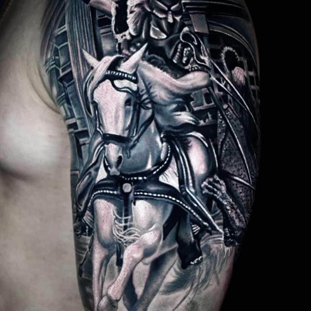 Black-and-gray upper arm tattoo of a rider on a horse with a theatrical mask and architectural background