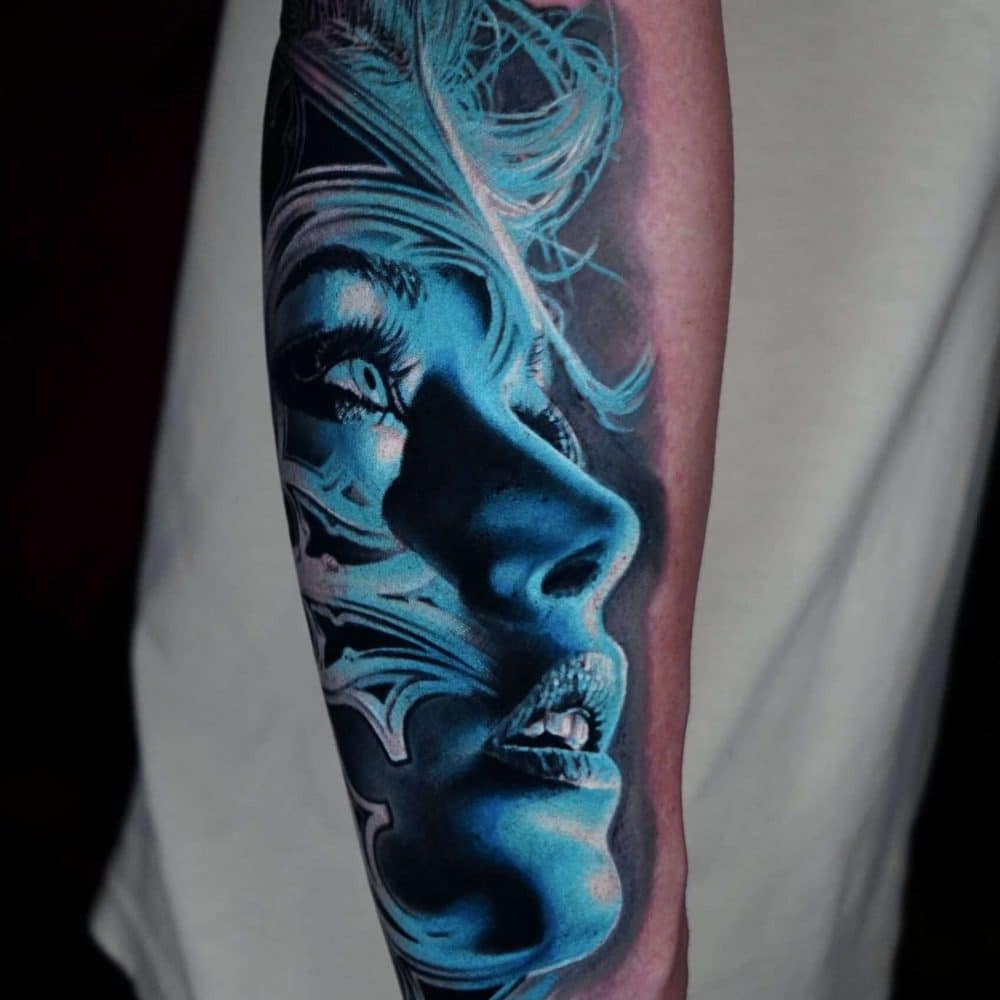 Blue-toned forearm tattoo of a woman's face with flowing hair and dramatic shading